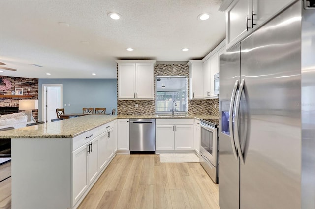 kitchen featuring appliances with stainless steel finishes, a peninsula, a sink, light wood-style floors, and tasteful backsplash