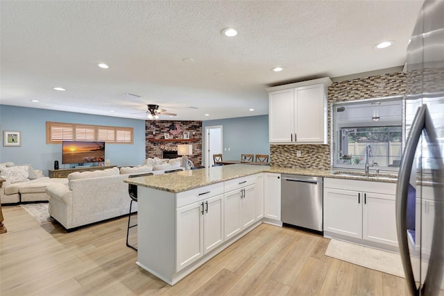 kitchen featuring a sink, appliances with stainless steel finishes, a ceiling fan, a peninsula, and a stone fireplace