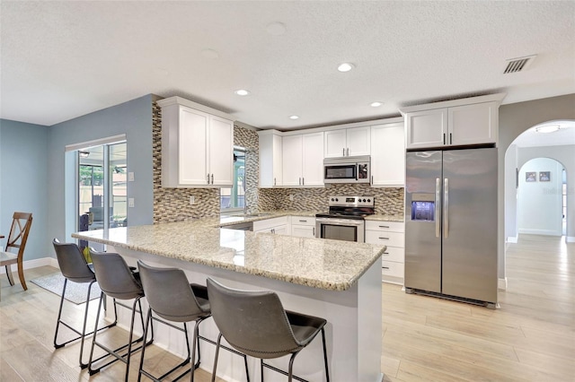 kitchen featuring appliances with stainless steel finishes, a peninsula, arched walkways, backsplash, and light wood-type flooring