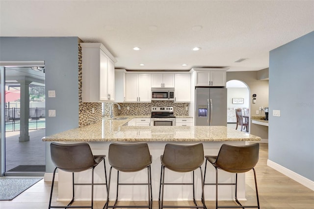 kitchen with appliances with stainless steel finishes, a peninsula, a sink, backsplash, and a kitchen bar