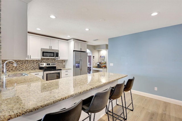 kitchen featuring stainless steel appliances, a sink, light stone countertops, a breakfast bar area, and a peninsula