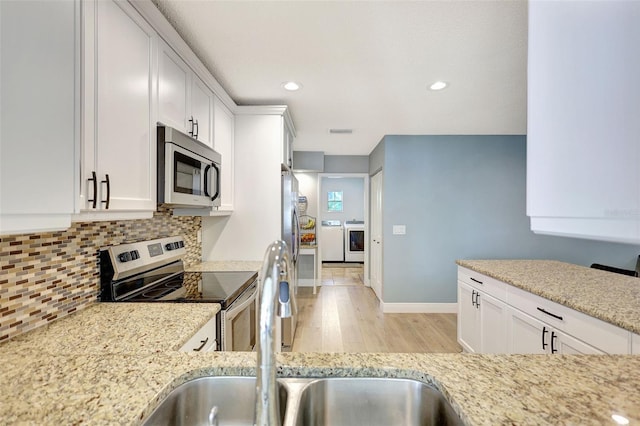 kitchen featuring appliances with stainless steel finishes, light wood finished floors, light stone counters, backsplash, and white cabinetry