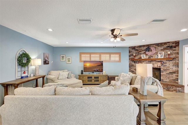 living area with a ceiling fan, a fireplace, a textured ceiling, light wood finished floors, and recessed lighting