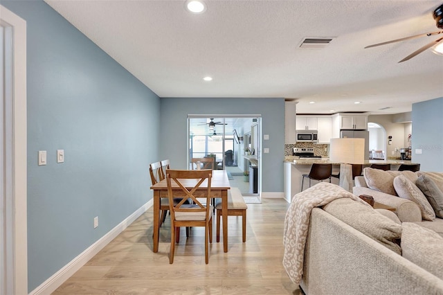 dining area with a ceiling fan, light wood-style floors, recessed lighting, arched walkways, and baseboards
