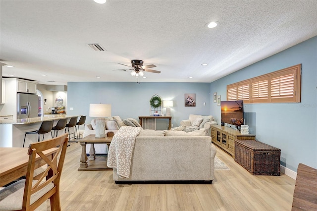 living area featuring a ceiling fan, light wood-type flooring, a textured ceiling, recessed lighting, and baseboards