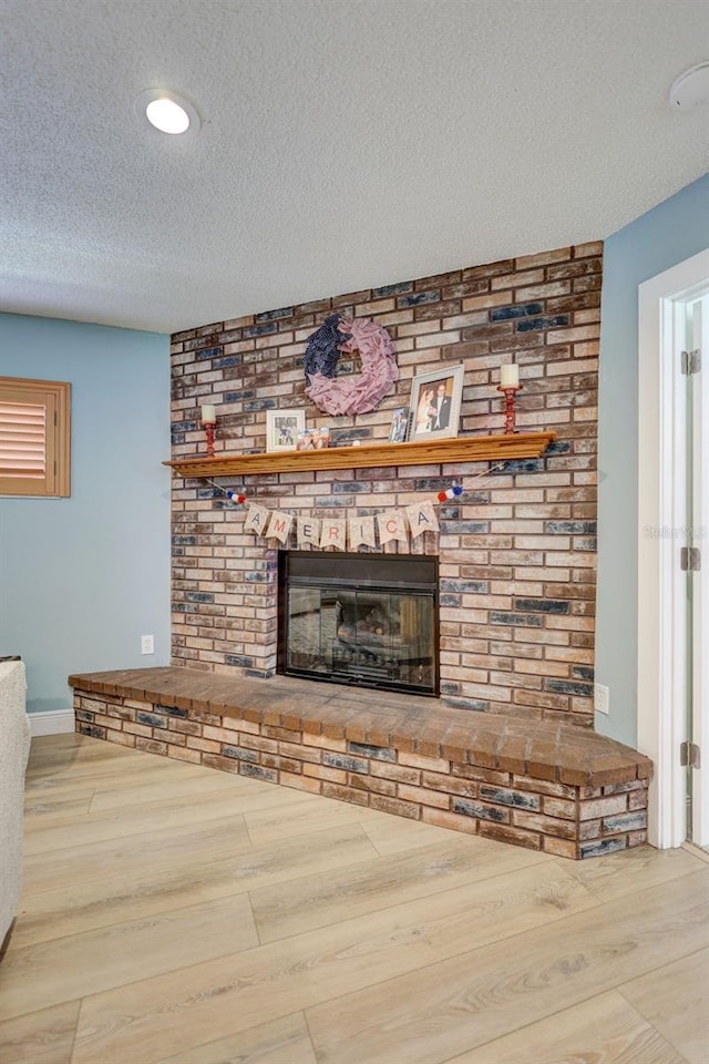 unfurnished living room with a textured ceiling, a brick fireplace, wood finished floors, and baseboards
