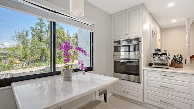 kitchen featuring stainless steel double oven, white cabinetry, light stone counters, recessed lighting, and light tile patterned floors
