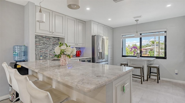 kitchen with stainless steel fridge, backsplash, a peninsula, baseboards, and light stone counters