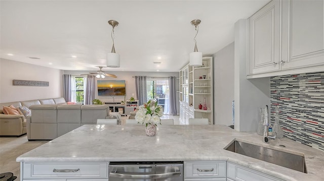 kitchen featuring open floor plan, a sink, tasteful backsplash, a peninsula, and light stone counters