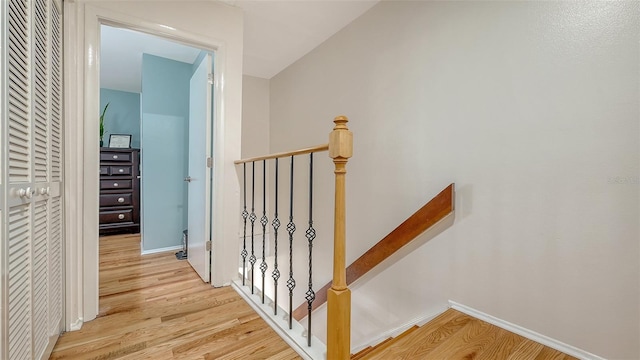 hall featuring an upstairs landing, light wood-style flooring, and baseboards