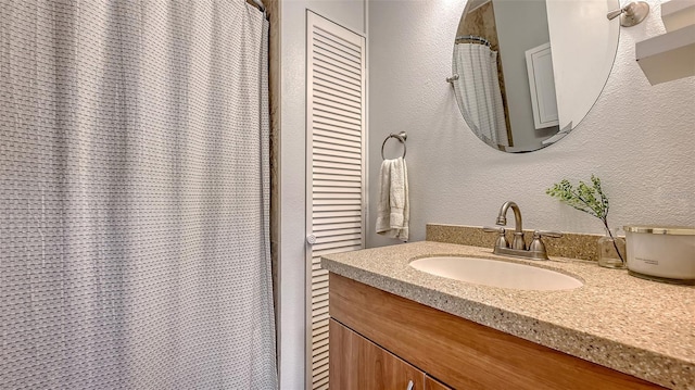 full bath featuring a textured wall and vanity