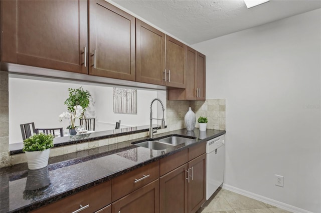 kitchen with a sink, white dishwasher, dark stone countertops, decorative backsplash, and baseboards