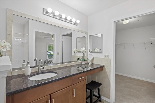 bathroom featuring a spacious closet, a ceiling fan, vanity, a tile shower, and tile patterned flooring