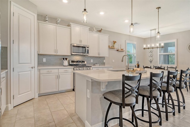 kitchen featuring appliances with stainless steel finishes, a sink, tasteful backsplash, light countertops, and a kitchen island with sink