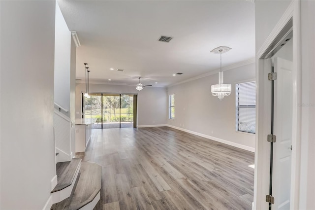 unfurnished living room with ceiling fan, light wood-type flooring, ornamental molding, a chandelier, and baseboards