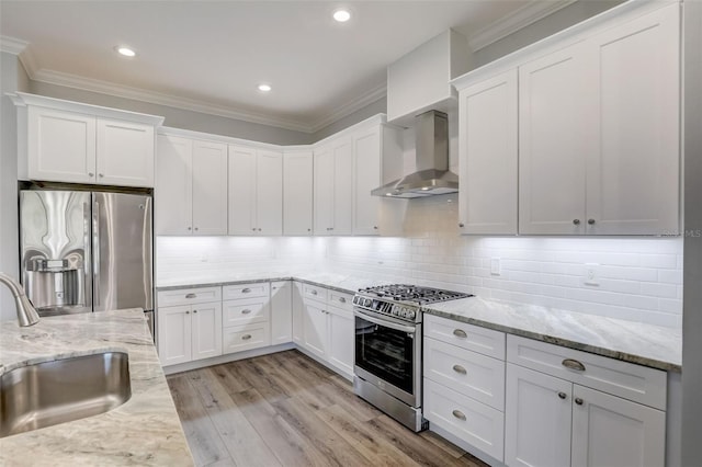 kitchen with stainless steel appliances, wall chimney exhaust hood, a sink, crown molding, and white cabinets