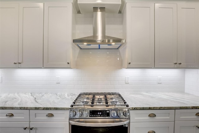kitchen featuring stainless steel gas range oven, wall chimney exhaust hood, backsplash, light stone countertops, and white cabinets