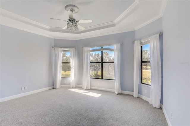 carpeted empty room featuring a raised ceiling, crown molding, ceiling fan, and baseboards