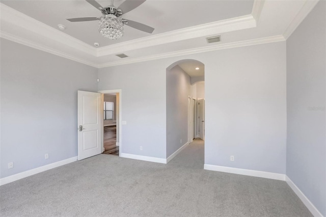 carpeted spare room featuring a tray ceiling, arched walkways, crown molding, a ceiling fan, and baseboards