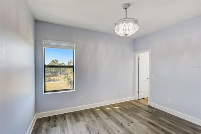 spare room with a chandelier, baseboards, and wood finished floors