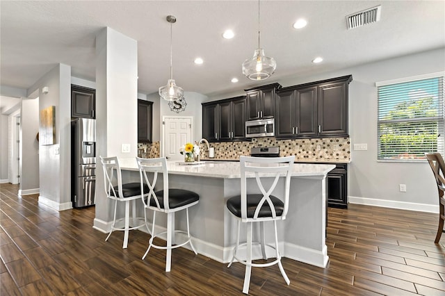 5805 49th Ct E, Ellenton, FL 34222 - kitchen featuring appliances with stainless steel finishes, tasteful backsplash, dark wood-type flooring, a center island with sink, and a kitchen bar