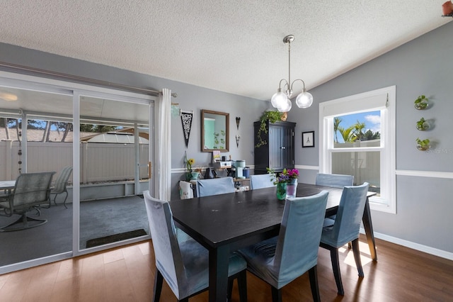 dining area with wood finished floors, healthy amount of natural light, a textured ceiling, a chandelier, and vaulted ceiling