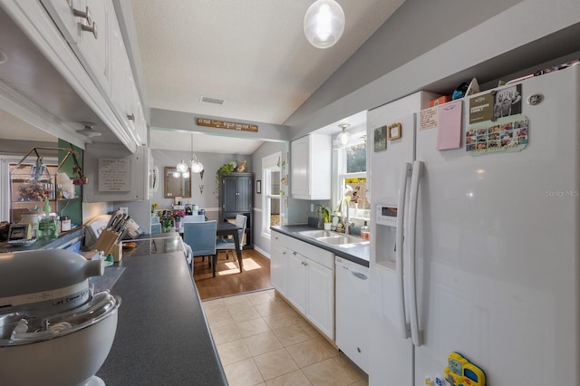 kitchen featuring white appliances, a sink, white cabinets, dark countertops, and vaulted ceiling