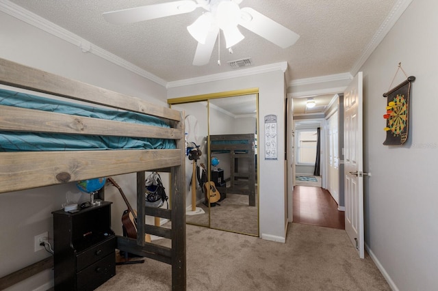 carpeted bedroom with a closet, ornamental molding, a textured ceiling, a ceiling fan, and baseboards