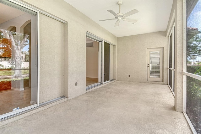 unfurnished sunroom with a textured wall, ceiling fan, and tile patterned floors