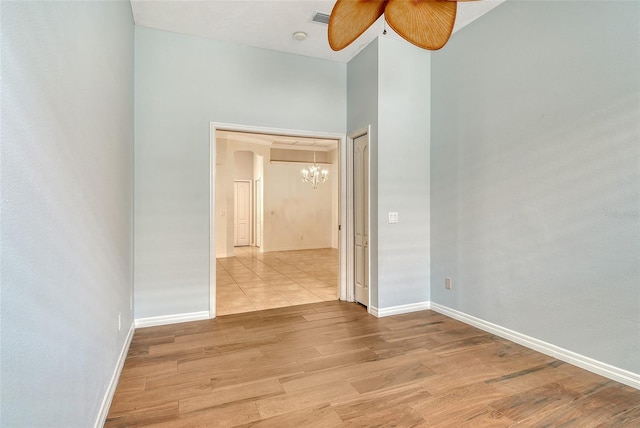unfurnished room featuring a chandelier, light wood-style flooring, a ceiling fan, and baseboards