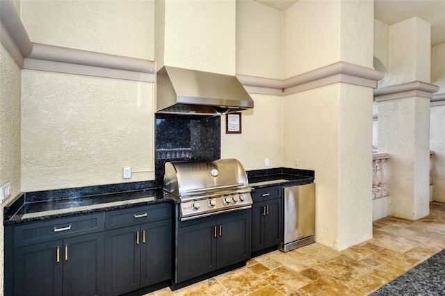 kitchen featuring fridge, a textured wall, stone finish floors, dark countertops, and wall chimney exhaust hood