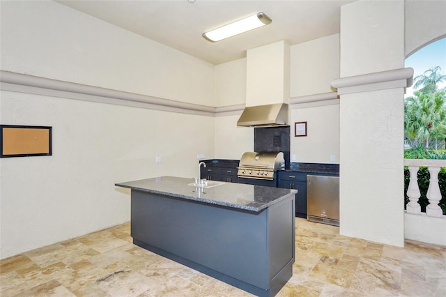 kitchen with refrigerator, a sink, stone finish flooring, and wall chimney exhaust hood