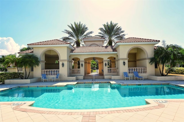 back of house with stucco siding, a community pool, a patio area, and a tiled roof
