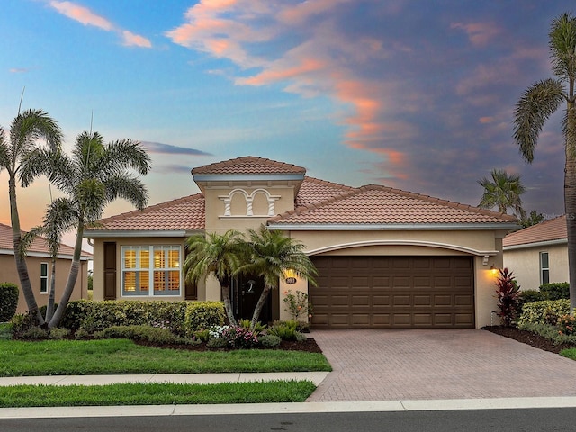 mediterranean / spanish house featuring an attached garage, decorative driveway, a tile roof, and stucco siding