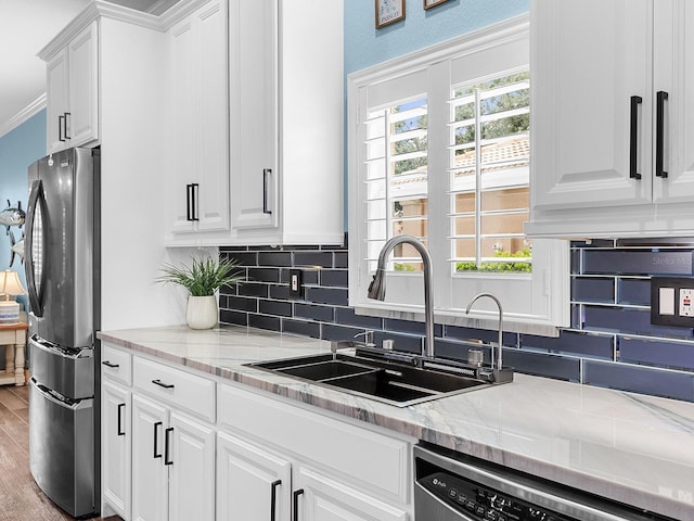 kitchen featuring a sink, stainless steel appliances, backsplash, white cabinetry, and ornamental molding