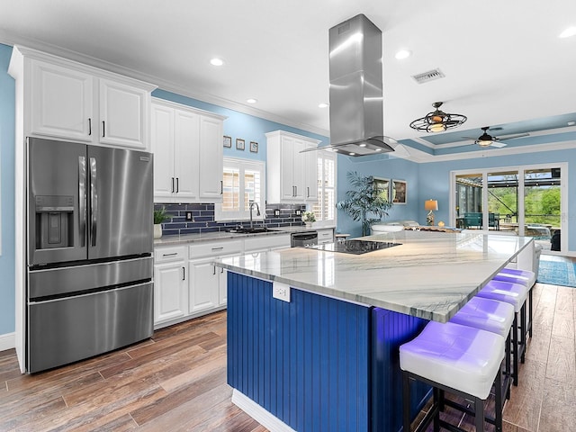 kitchen featuring stainless steel fridge, island exhaust hood, ceiling fan, plenty of natural light, and ornamental molding