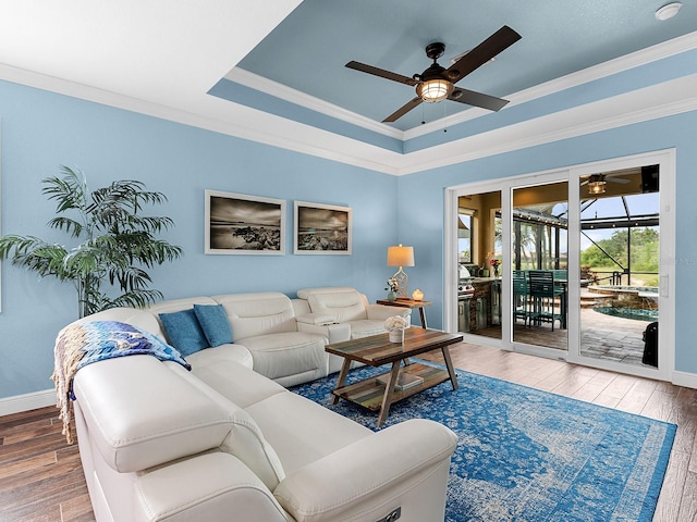 living room featuring ceiling fan, wood finished floors, baseboards, crown molding, and a tray ceiling