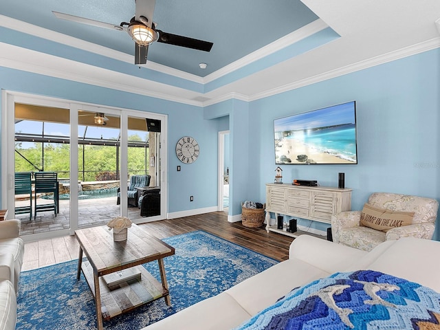 living room with a ceiling fan, wood finished floors, ornamental molding, baseboards, and a raised ceiling