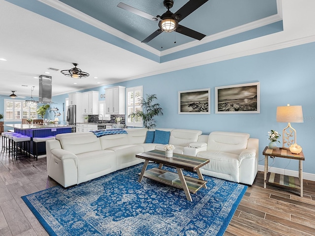 living area featuring a ceiling fan, crown molding, wood finished floors, a tray ceiling, and recessed lighting