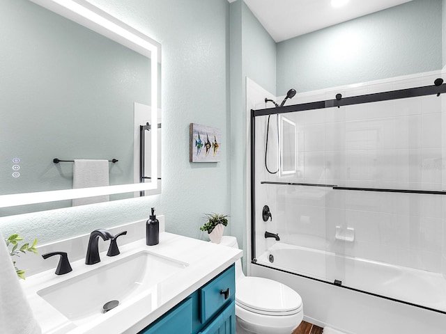 full bath with a textured wall, toilet, bath / shower combo with glass door, and vanity