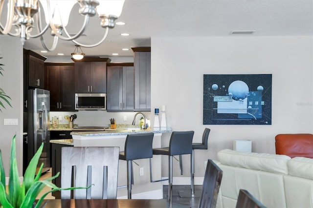 3430 77th St W Unit 103, Bradenton, FL 34209 - kitchen featuring appliances with stainless steel finishes, a chandelier, a peninsula, light stone counters, and dark brown cabinetry
