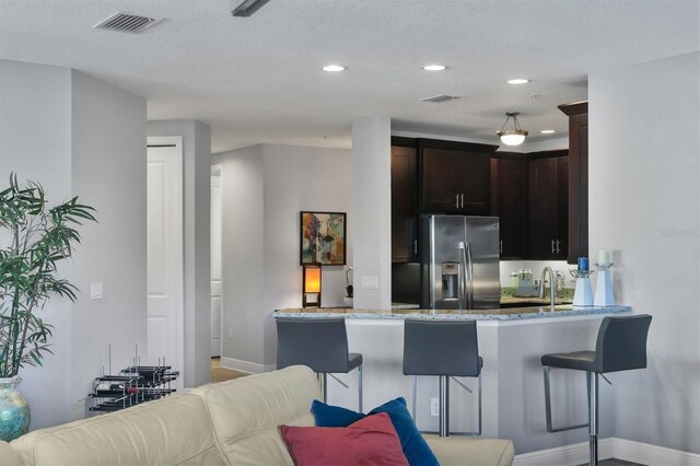 3430 77th St W Unit 103, Bradenton, FL 34209 - kitchen with stainless steel refrigerator with ice dispenser, baseboards, light stone counters, dark brown cabinets, and recessed lighting