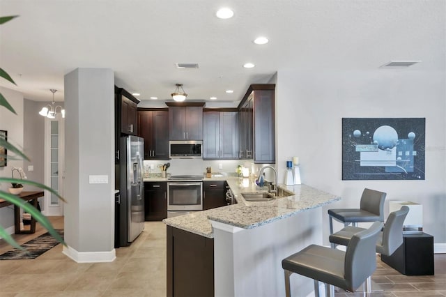 3430 77th St W Unit 103, Bradenton, FL 34209 - kitchen featuring appliances with stainless steel finishes, a sink, a peninsula, light stone countertops, and dark brown cabinets