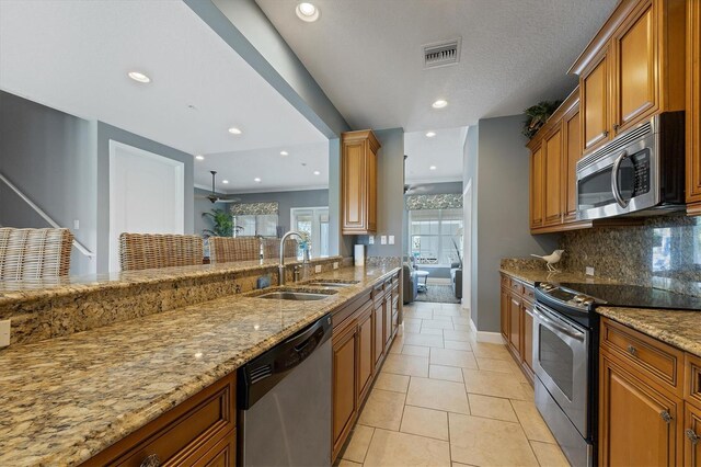 3430 77th St W Unit 103, Bradenton, FL 34209 - kitchen with stainless steel appliances, a sink, brown cabinetry, decorative backsplash, and light stone counters