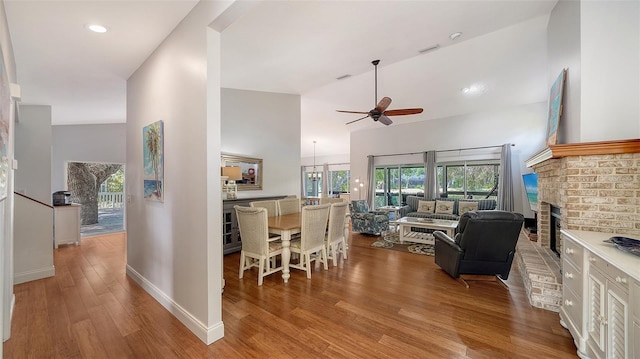living area featuring ceiling fan, wood finished floors, a brick fireplace, high vaulted ceiling, and baseboards