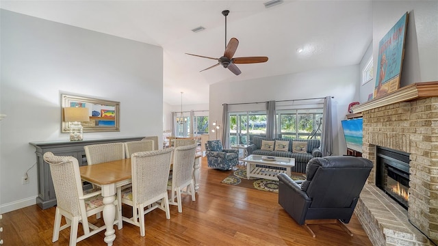 dining space with a brick fireplace, a ceiling fan, wood finished floors, a chandelier, and lofted ceiling