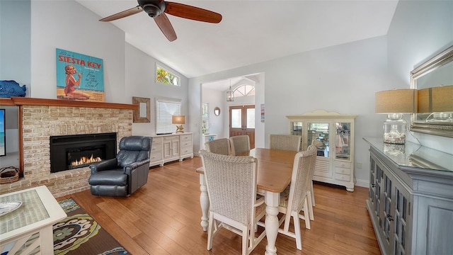 dining area with high vaulted ceiling, a ceiling fan, a fireplace, and wood finished floors