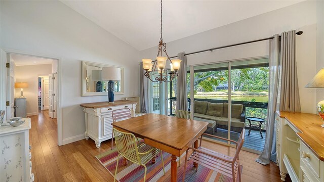dining room featuring a chandelier, light wood finished floors, baseboards, and high vaulted ceiling
