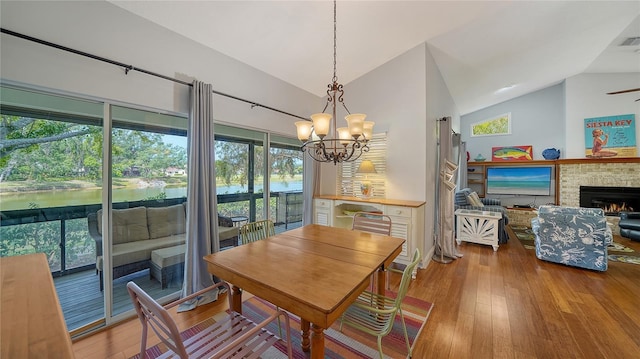 dining area featuring vaulted ceiling, a chandelier, hardwood / wood-style flooring, a brick fireplace, and a ceiling fan