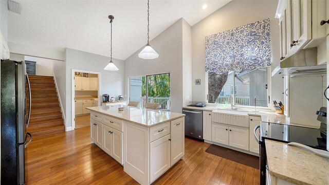 kitchen featuring freestanding refrigerator, stainless steel dishwasher, light wood finished floors, white cabinets, and high vaulted ceiling